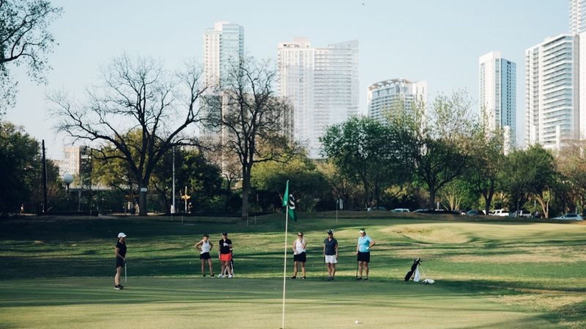 Golfers on a green at Butler Pitch & Putt with the Austin skyline behind the course.